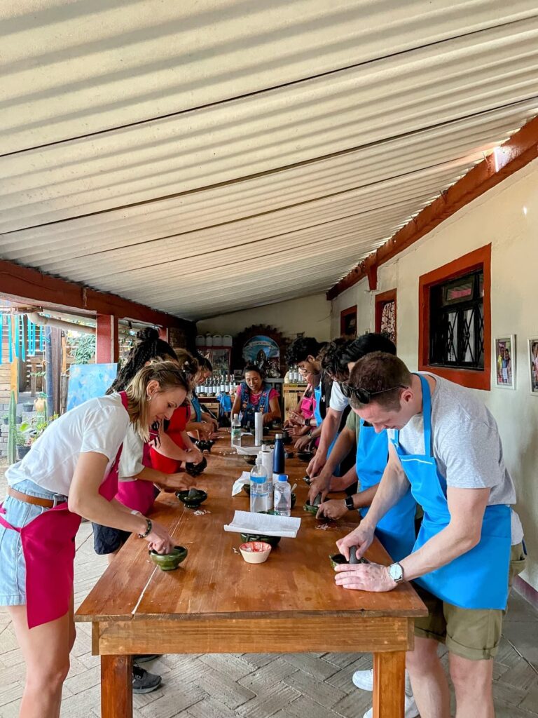 A group of people standing around a table preparing food. Wondering how to make friends while traveling solo? Cooking classes like this are a great option