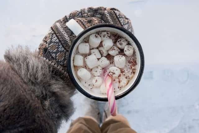 Mug of hot chocolate with marshmallows and candy cane in the snow