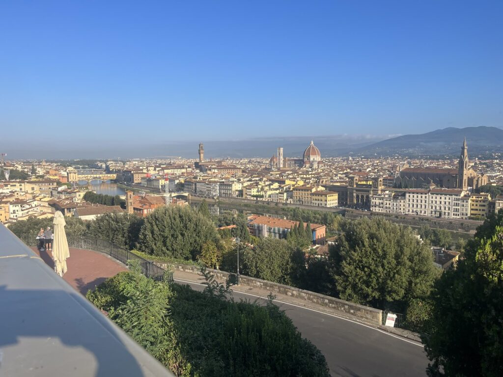 A panoramic view of Florence, Italy, taken from Piazzale Michelangelo, showing the iconic red dome of the Florence Cathedral, the Arno River, and the city's historic skyline with rolling hills in the distance. A stop to include during your 4 days in Florence.