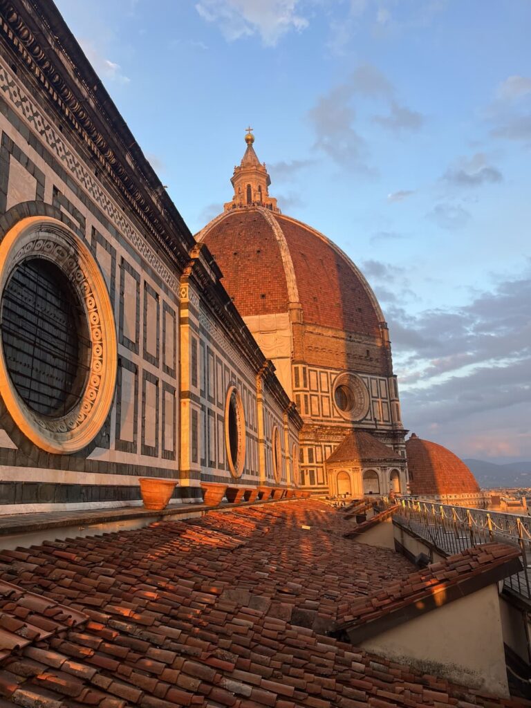 A dramatic, close-up side angle of the Florence Cathedral (Duomo) at golden hour, highlighting its detailed marble façade and massive terracotta dome.