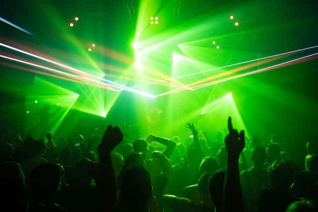 Nightclub with green lights and laser light flashing through with silhouettes of people's hands raised enjoying Tulum nightlife