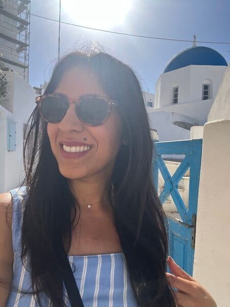 woman smiling wearing sunglasses with blue domed, white church behind her