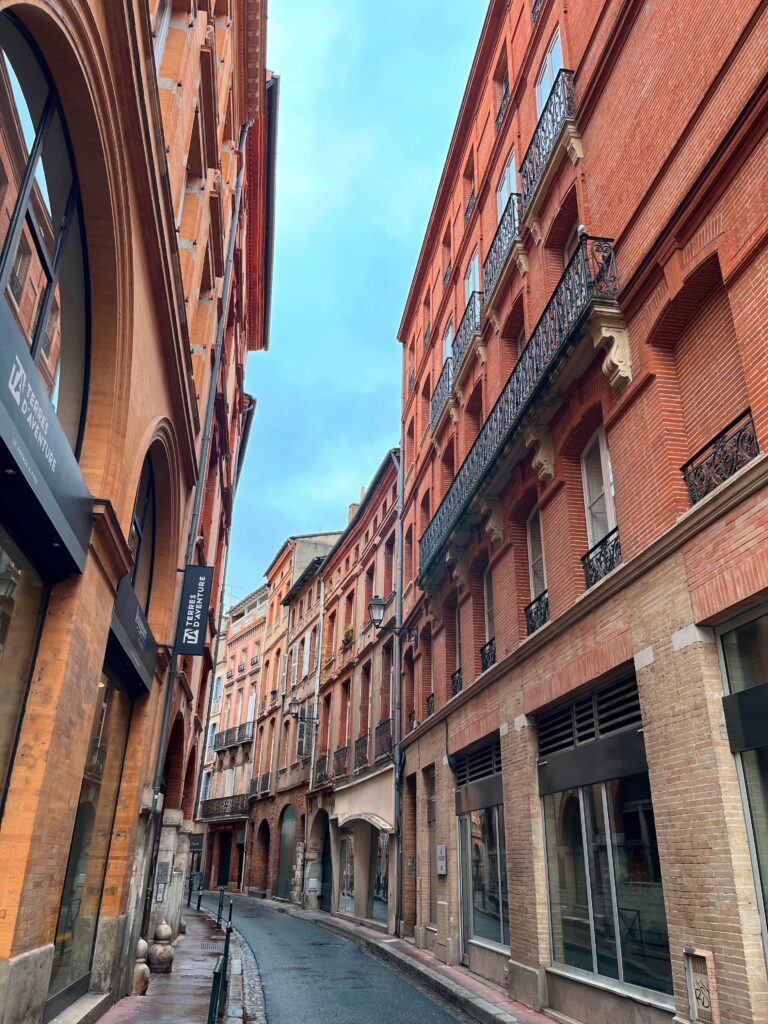 a narrow street in Toulouse with pink buildings on each side