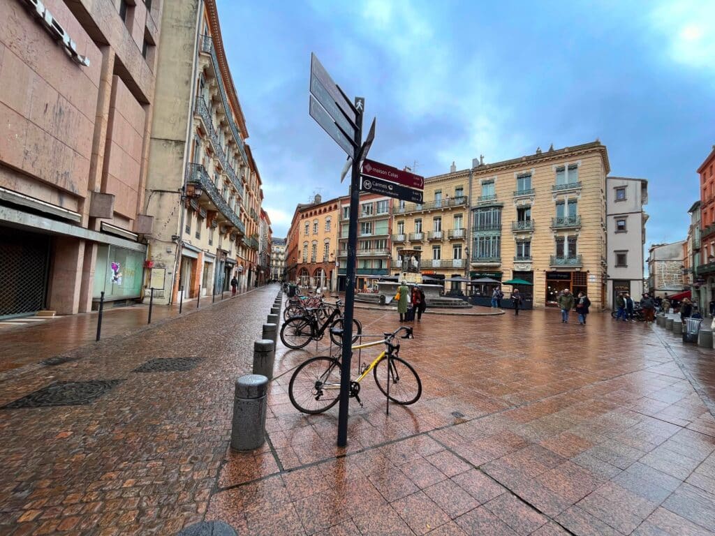 a square in toulouse with street signs and pinkish hued architecture