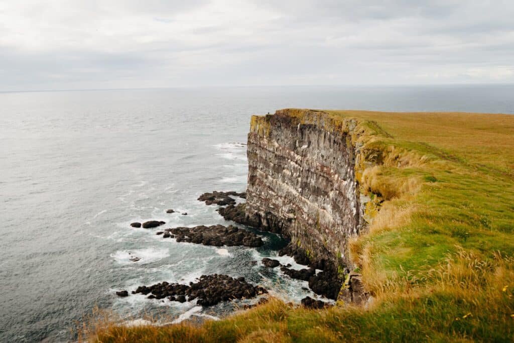 grassy, rock cliff standing over a body of water in Iceland