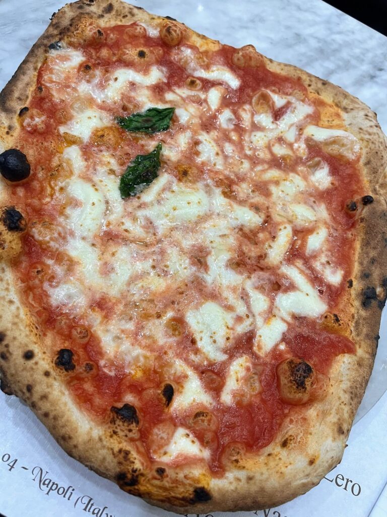 Close-up of a classic Neapolitan Margherita pizza with a golden, slightly charred crust, topped with melted mozzarella cheese, rich tomato sauce, and fresh basil leaves. Served on a marble surface.