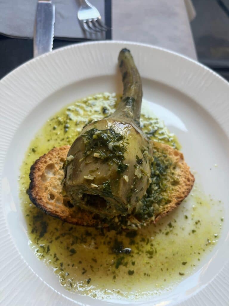 stewed artichoke atop toast on a plate, a dish you can try when visiting Rome in November