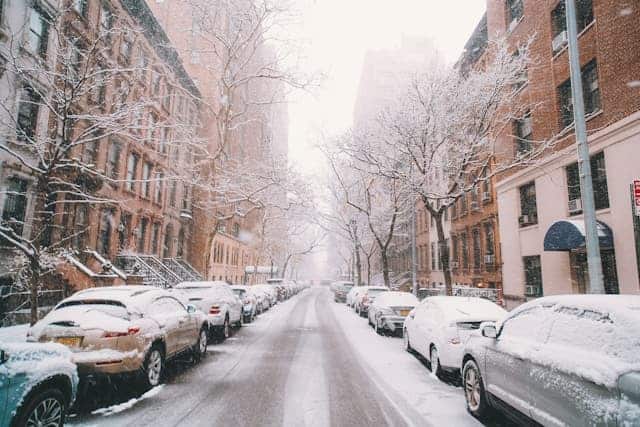 view of a street in new york in winter during snow with cars and buildings on each side