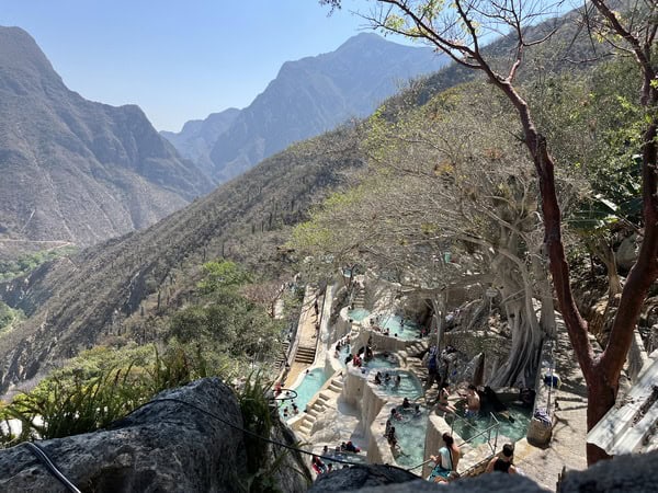 aerial view of hot spring pools of grutas de tolantono set against grassy mountain backdrop 