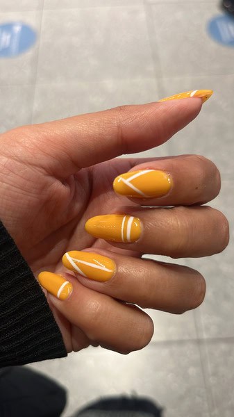 woman's painted fingernails, mustard yellow with simple white patterned, hand painted design