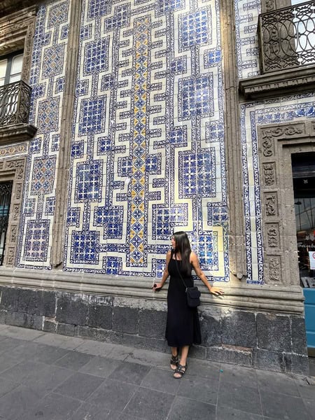 woman in black dress leaning against front of house of blue and white tiles in Mexico City