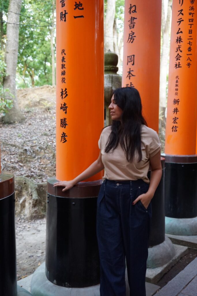 woman in beige tee shirt and dark jeans in front of an orange pillar with Japanese letters written on it