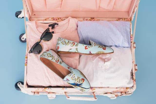 open suitcase with pink and purple packing cubes inside with a pair of black sunglasses and light blue, floral loafers on top of it