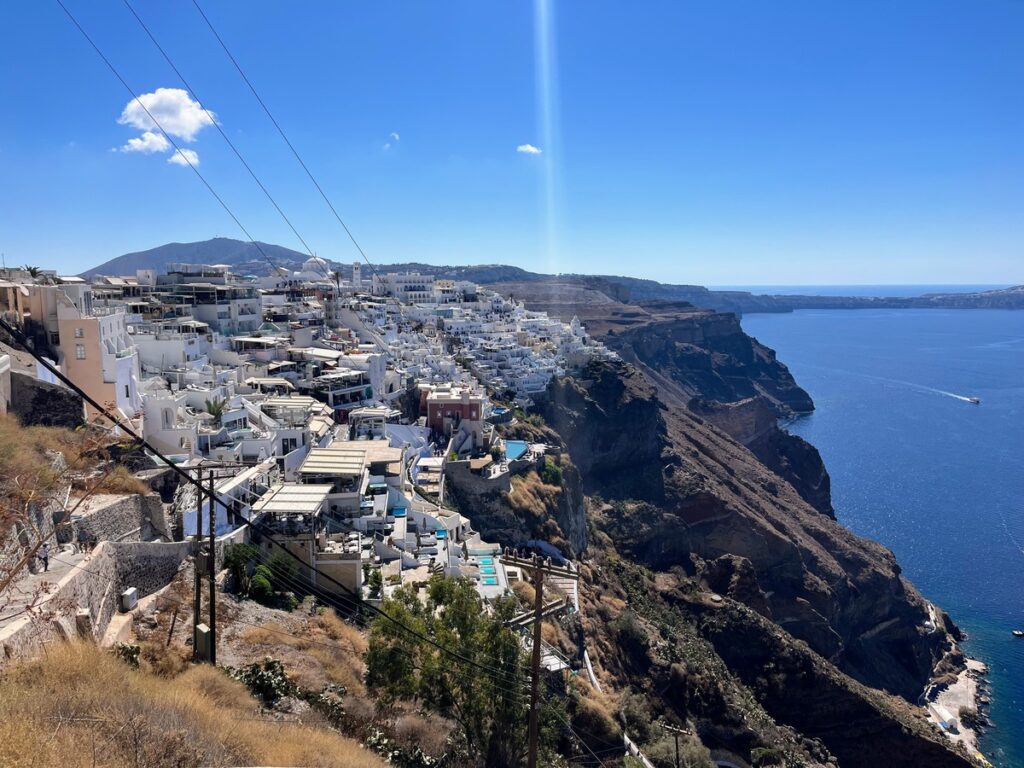 View of city built on cliffside on left side dotted with white buildings, blue sea on the other