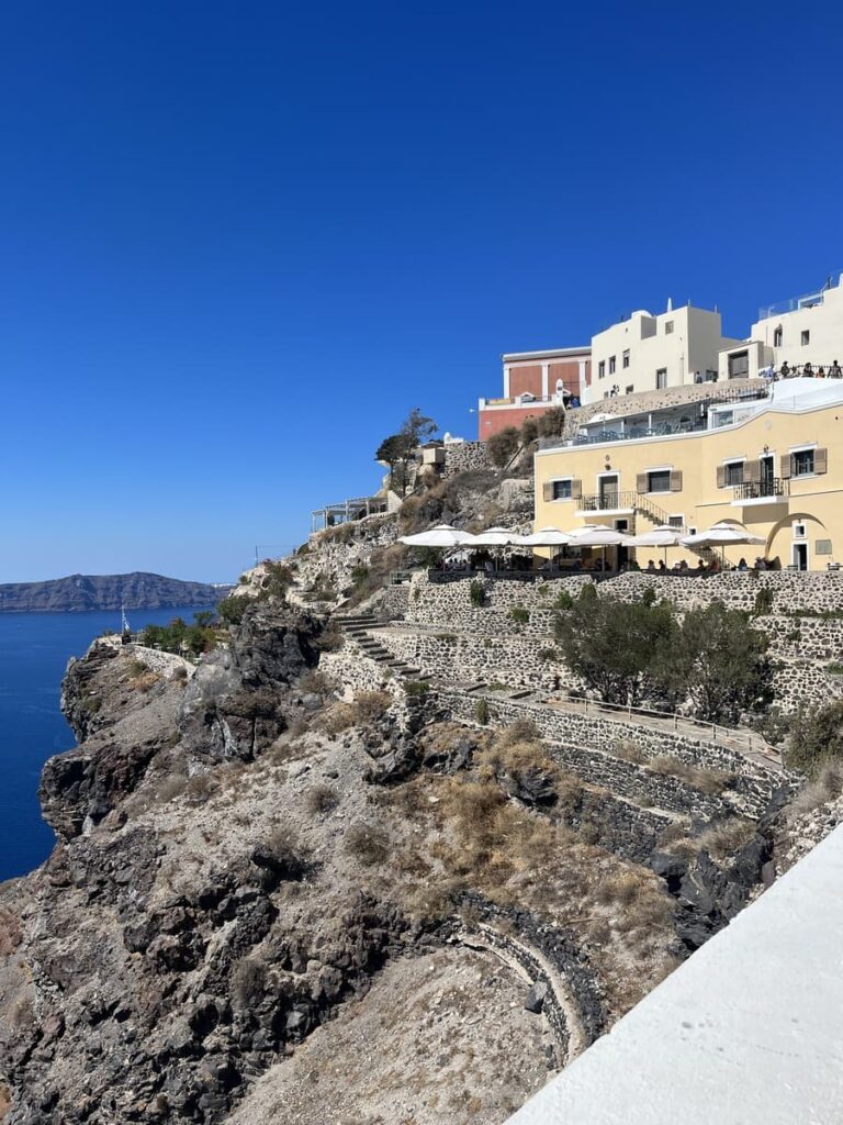 cliffside view of Santorini, with buildings on one side and sea on the other. when deciding what to wear in Santorini consider packing for the Fira-Oia hike as well