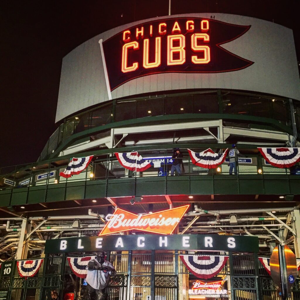 Front entrance of Wrigley Field stadium which opens during Spring in Chicago, seen at nighttime with the words Chicago Cubs lit up on a sign in red