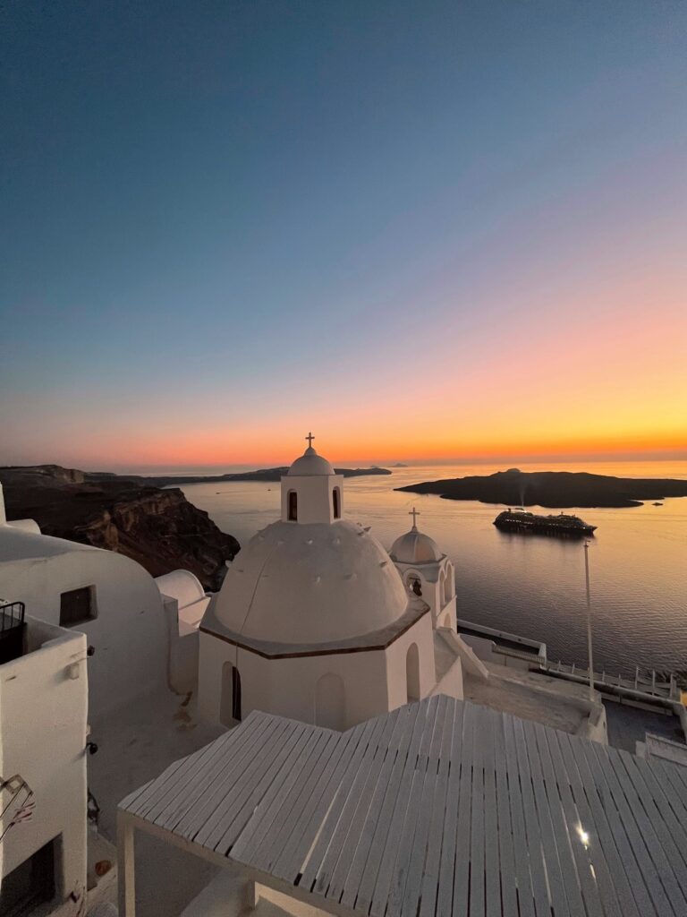 blue, pink and orange sky at sunset in background over the Mediterranean sea, with white church in foreground