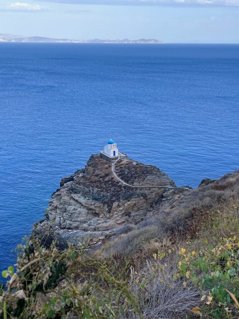 whitewashed church with blue dome atop a rocky inlet jutting into blue sea in Greece