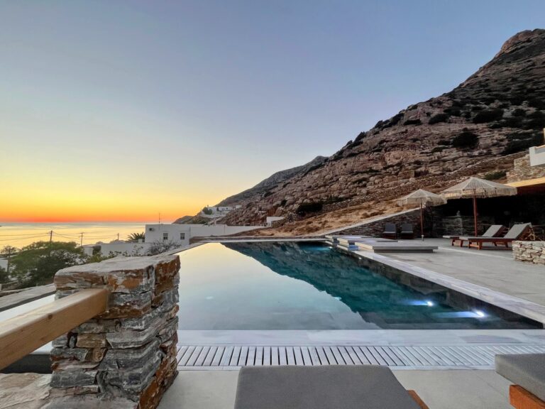 pool in foreground with a mountain rising to the right, and sun setting over sea on the left in the background