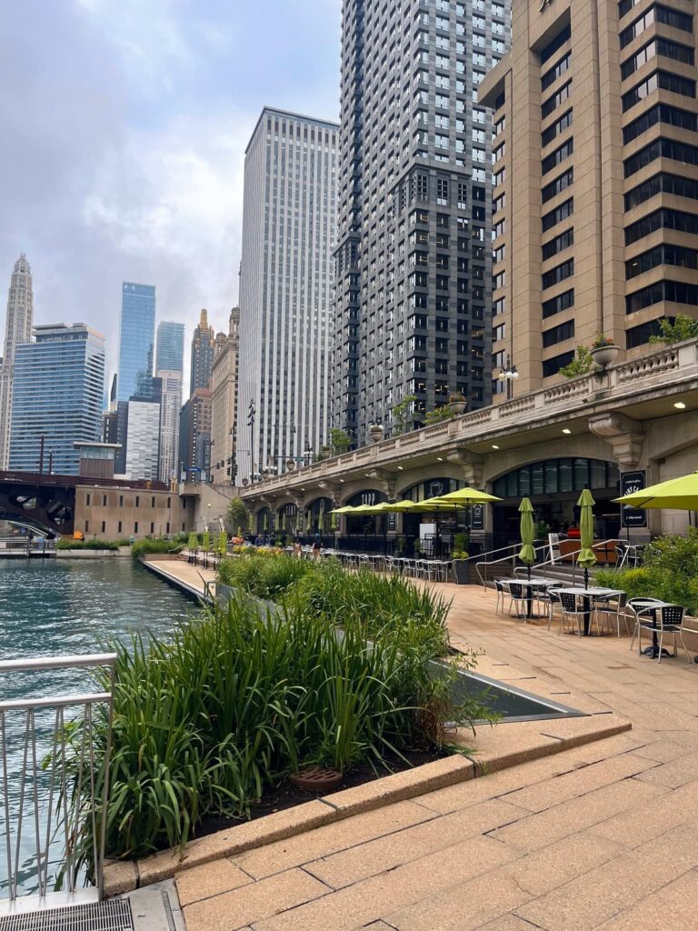 Riverside walkway with a restaurant on one side, lake on the other and surrounded by skyscrapers 
