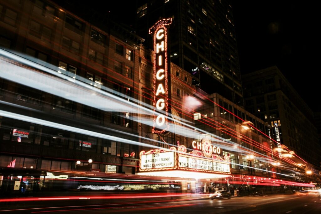 Nighttime shot of the iconic Chicago Theatre with bright red lights and a long exposure effect capturing streaks of moving lights from cars on the street.