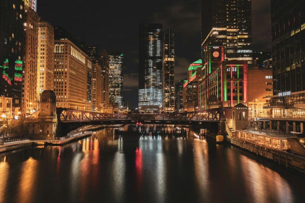 Chicago River at night with buildings lit in holiday colors, reflecting off the water and bridges. A scene from Christmas in Chicago