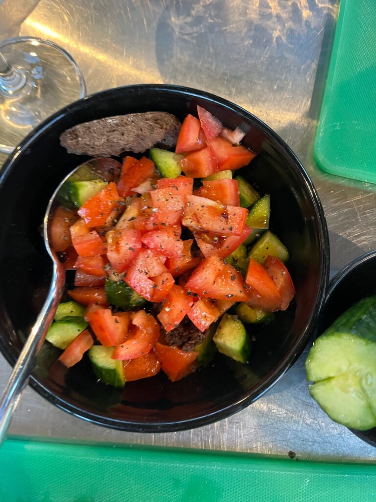 Bowl of chopped tomatoes and cucumbers mixed with herbs and olive oil served with pieces of bread on a kitchen counter.