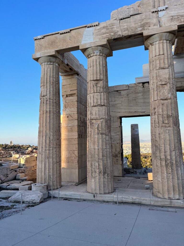 Ancient marble columns and stone structure at a historic site in Athens with the city visible through the openings and a clear blue sky above.