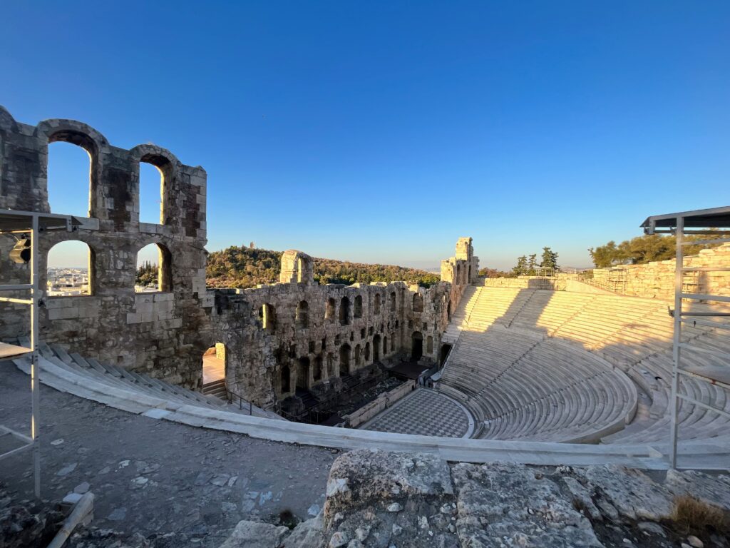 Stone amphitheater with curved seating and arched ruins overlooking Athens under a clear sky showcasing one of the historic sites to consider when planning how many days in Athens.