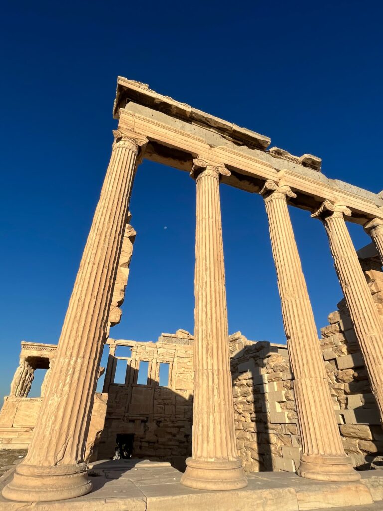Tall ancient stone columns of a Greek temple rise against a bright blue sky showcasing historic ruins to visit when deciding how many days in Athens.