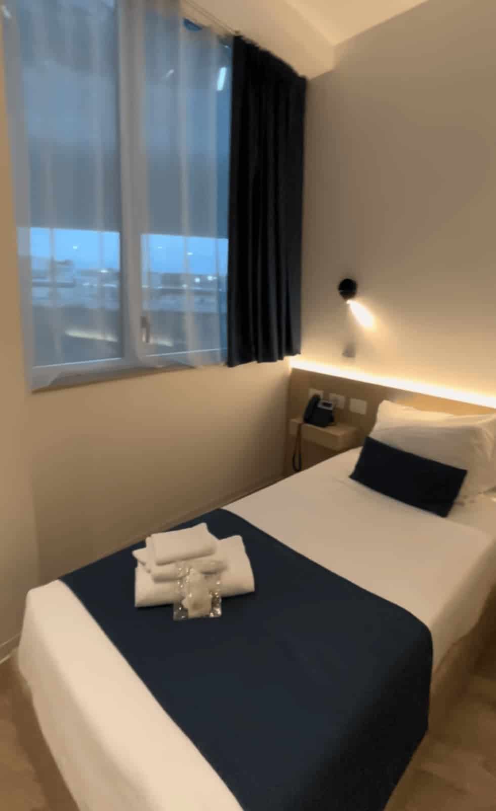 Walk in hotel shower with dark blue mosaic tiles and a glass partition. The shower has a large overhead rainfall fixture and a handheld shower head.